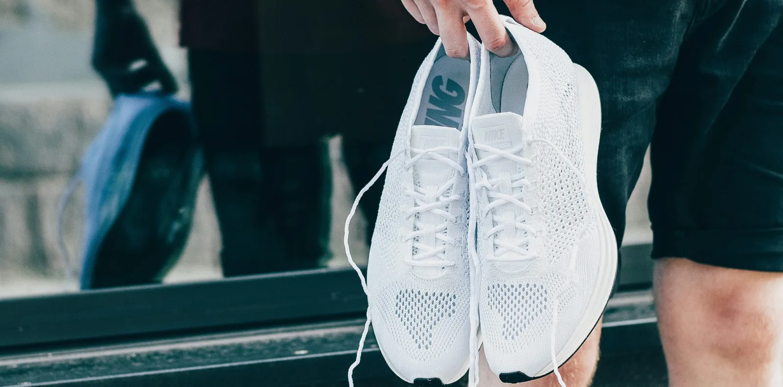 A hand holding a pair of white lightweight sneakers