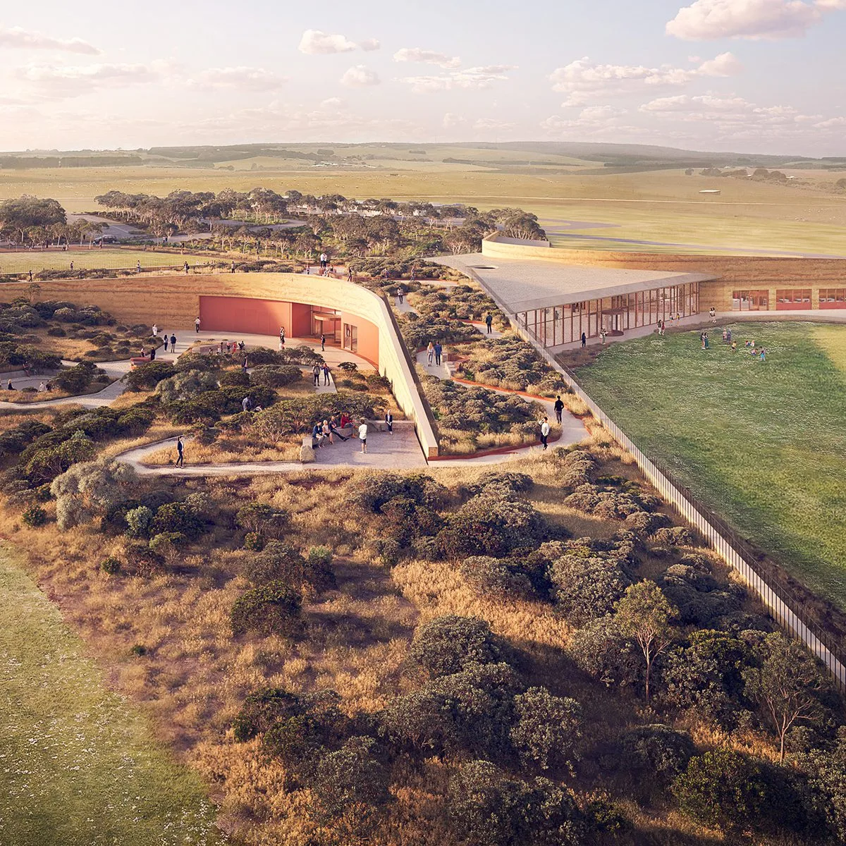 Aerial view of the Twelve Apostles visitor centre, a low curved building in earthy tones set into coastal heathland with walking paths and open farmland beyond