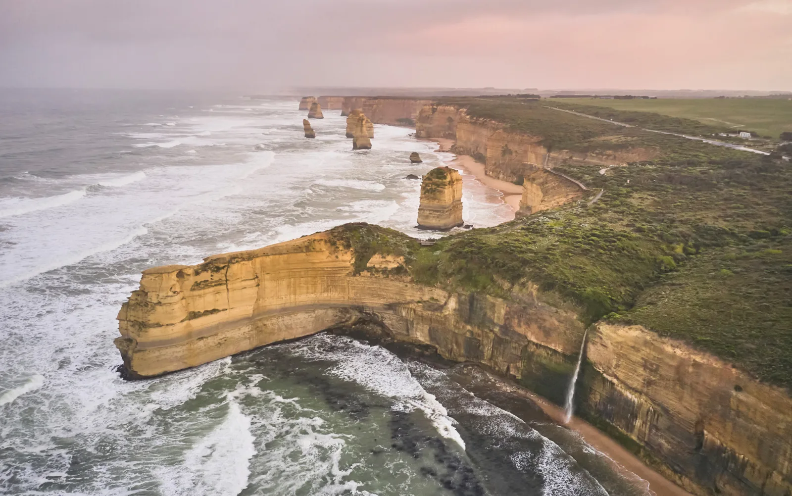 Aerial view of the Twelve Apostles coastline at dusk, with limestone stacks and rugged cliffs stretching into the distance and white surf below