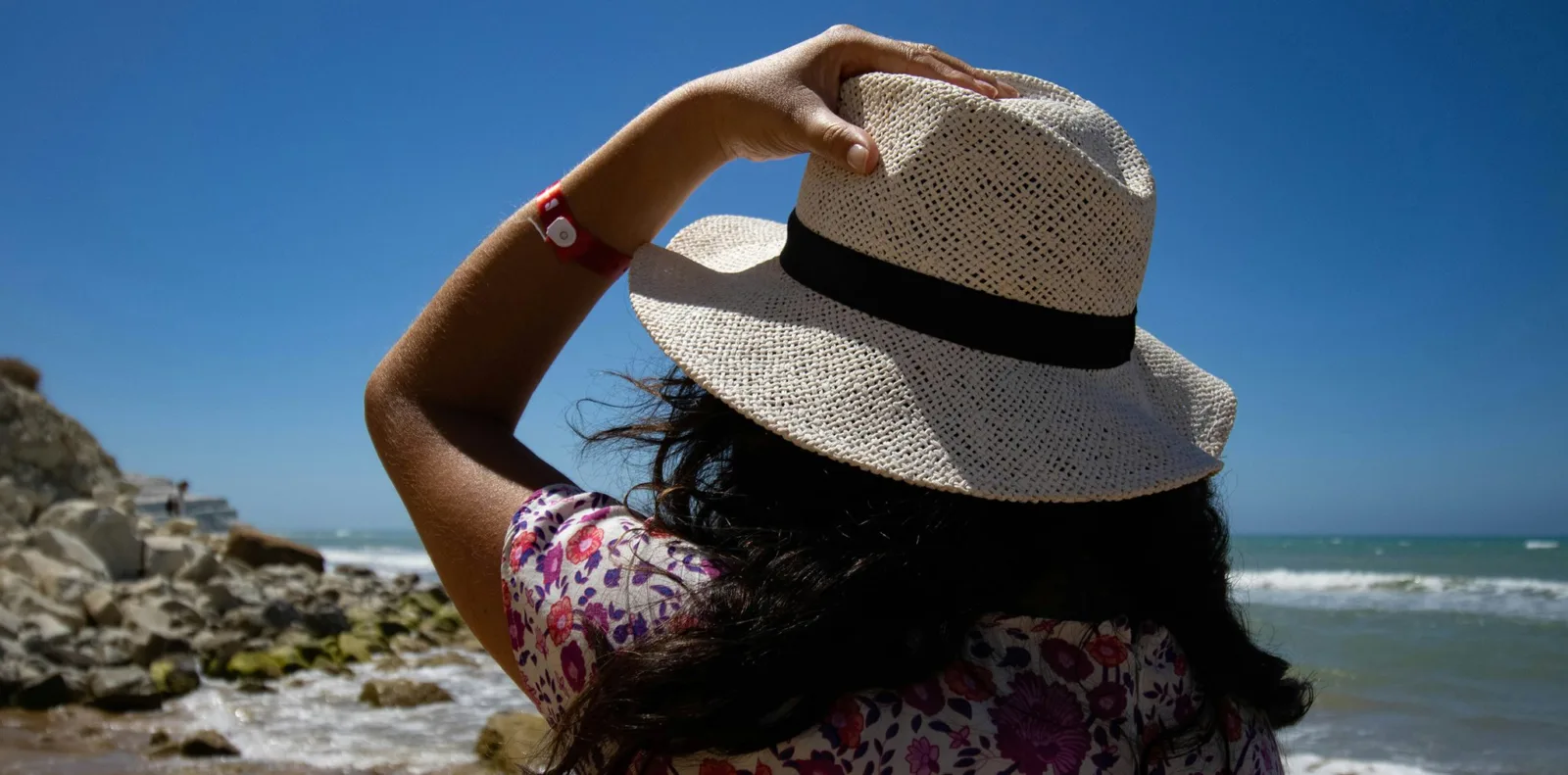 A woman in a wide-brimmed sun hat looking out over the ocean on a bright sunny day