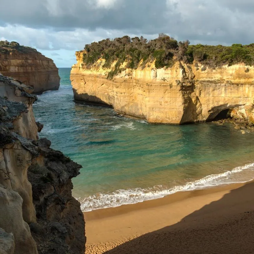 Turquoise water flowing into a sheltered sandy cove framed by golden limestone cliffs
