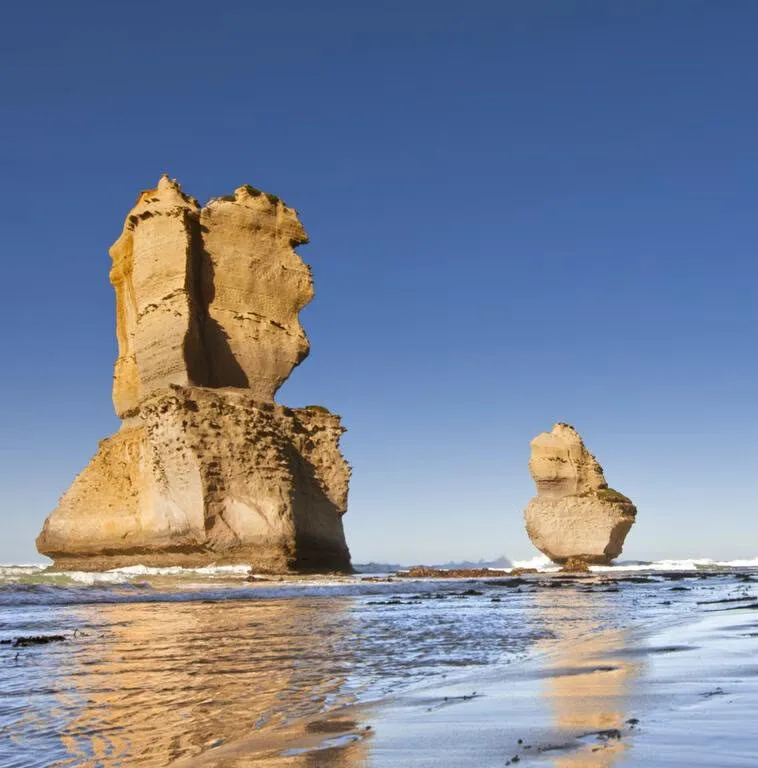 Two sunlit limestone stacks rising from the shallows under a clear blue sky