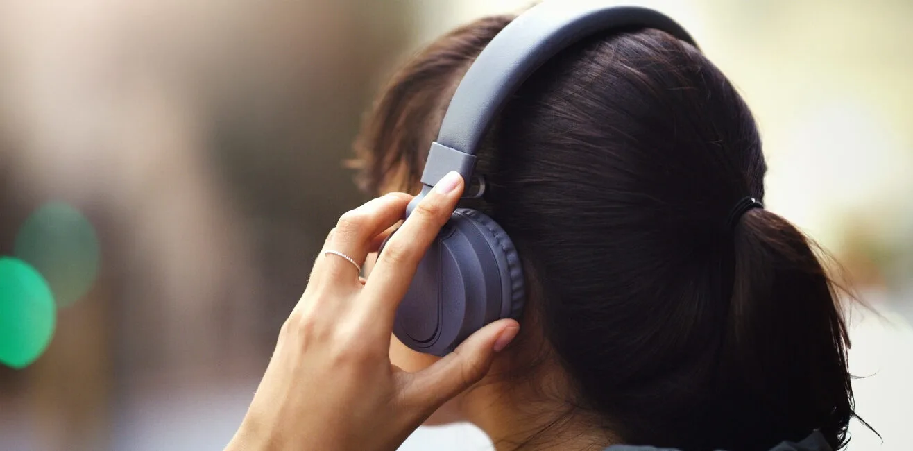 A person wearing over-ear headphones, adjusting them with one hand